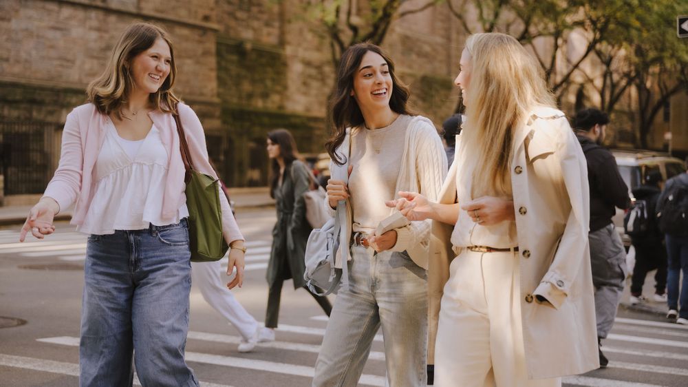 Three students chat and walk across the street
