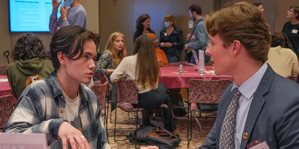 Two male presenting students engaging in conversation