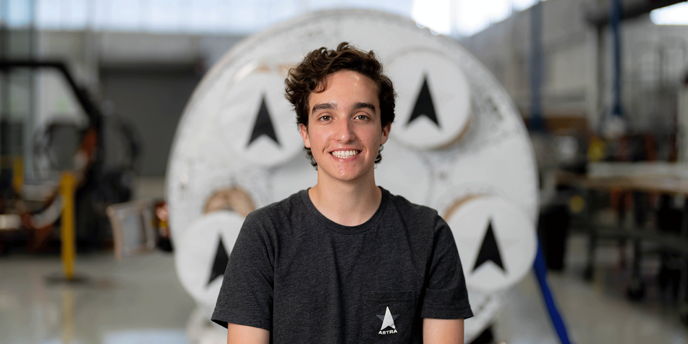 David Adipietro, pictured in front of Astra’s Rocket, named “Rocket 3.” He is wearing a black t-shirt and smiling.
