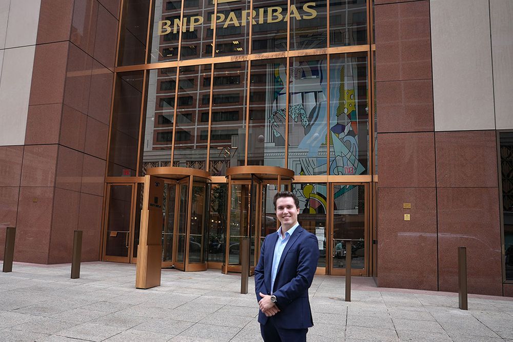 A student wearing a suit standing in front of an office building.