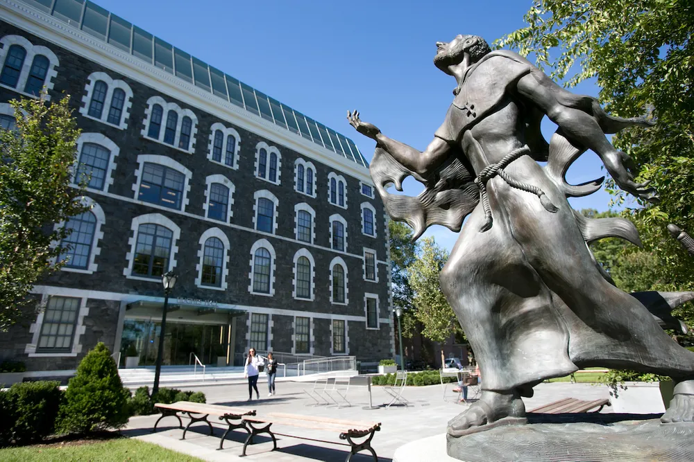 The exterior of Hughes Hall during the summer with a statue of Saint Ignatius in the foreground.