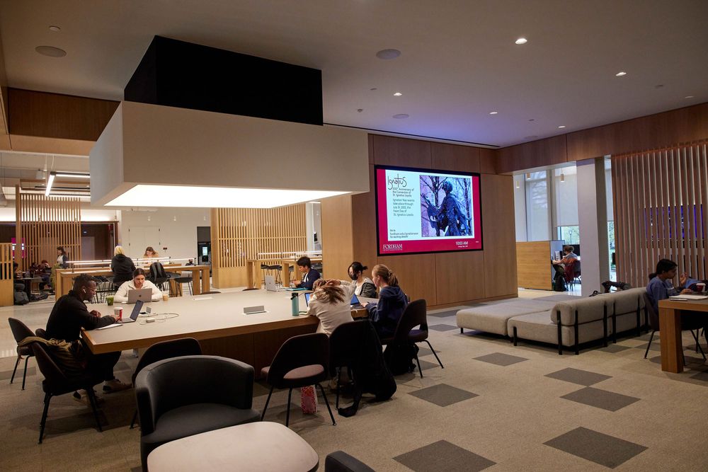 Several students study at a large square table in the McShane Center at Rose Hill