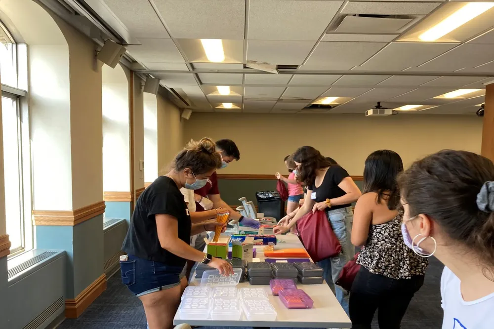 Students standing together around a table assembling backpacks to donate.