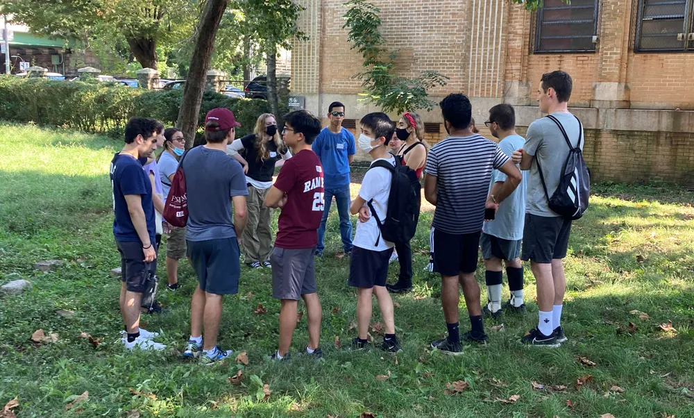 Students standing in a circle in a park with grass waiting to help clean up the park.