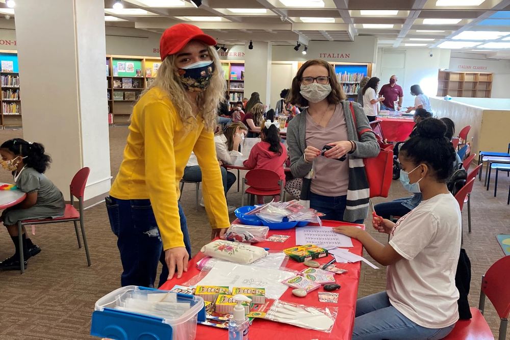 Two students standing around a table smiling with masks on with crafts on the table.