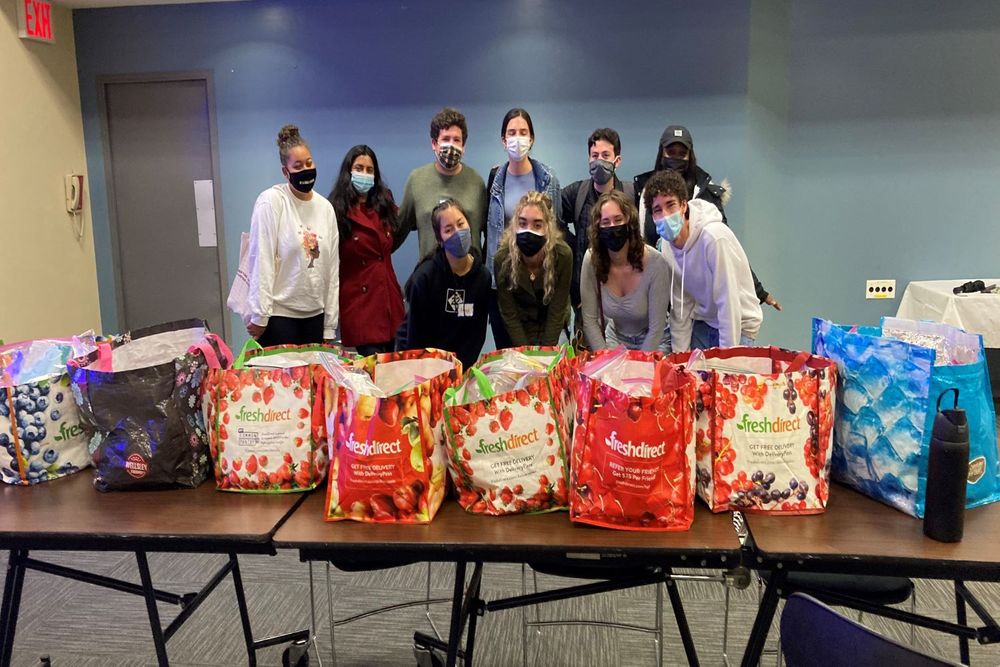 Students posing for group picture with two rows of students and a table with grocery bags on them preparing for a service project.