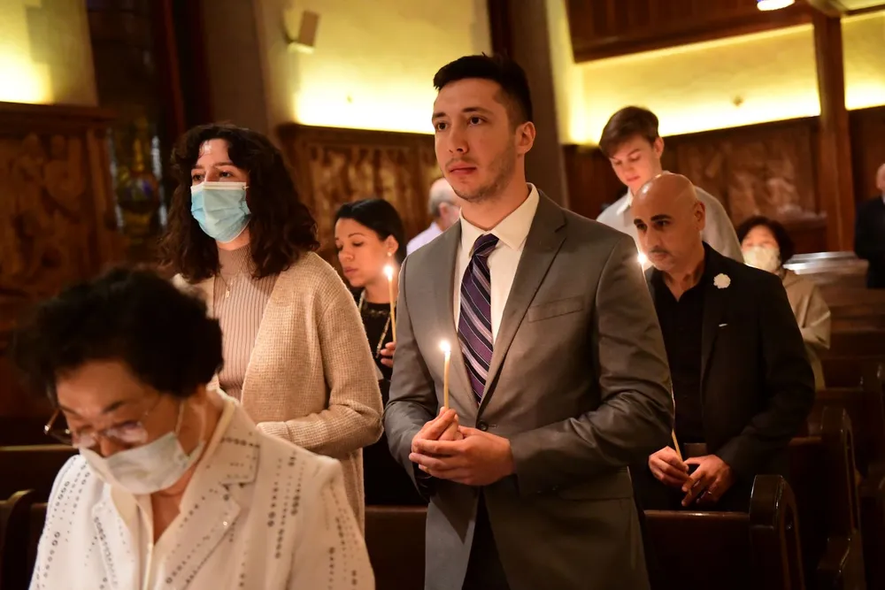 People standing at Mass in the University church holding candles.