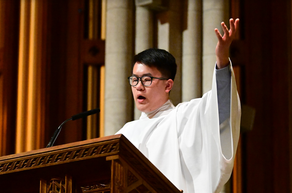 A student raising their hand at the podium in the University Church singing.
