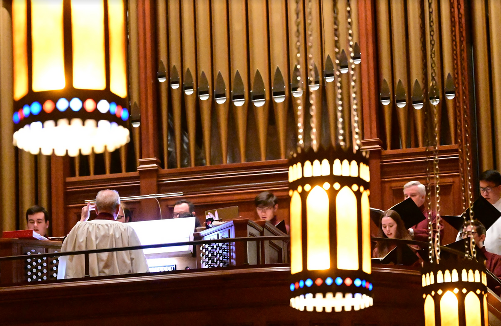 The Church Choir singing together with a piano and music director directing in the University Church.