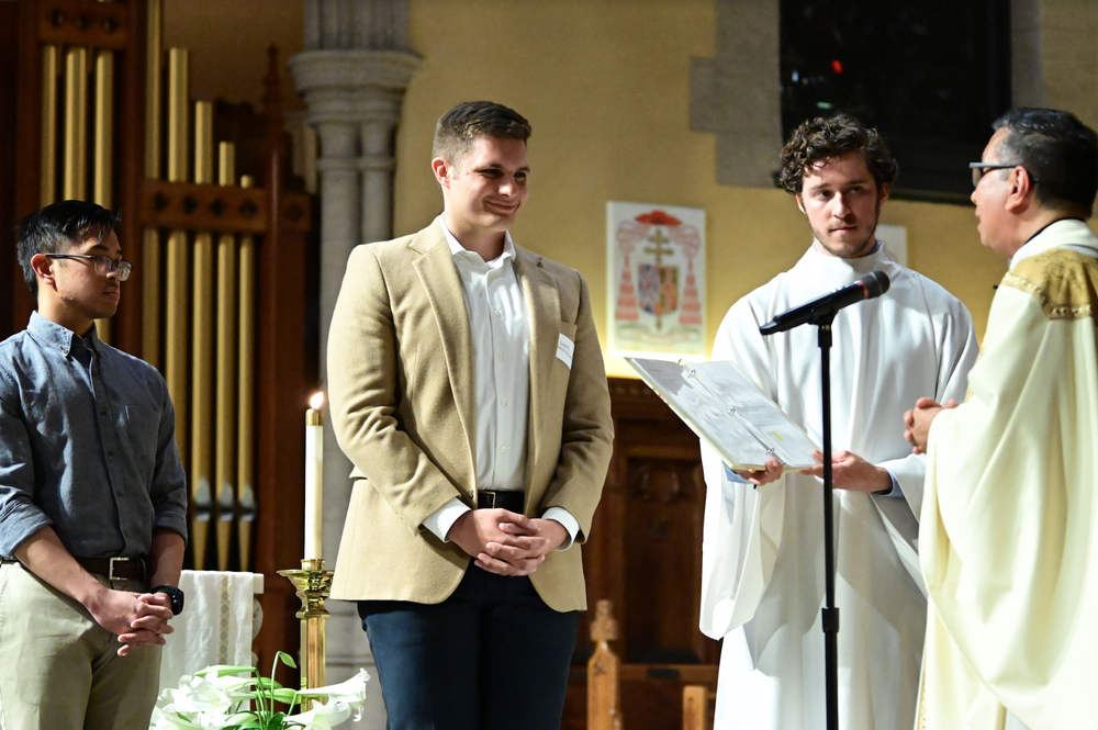 A student stands at the front of the University Church as he is blessed by the priest as a candidate for their sacrament.