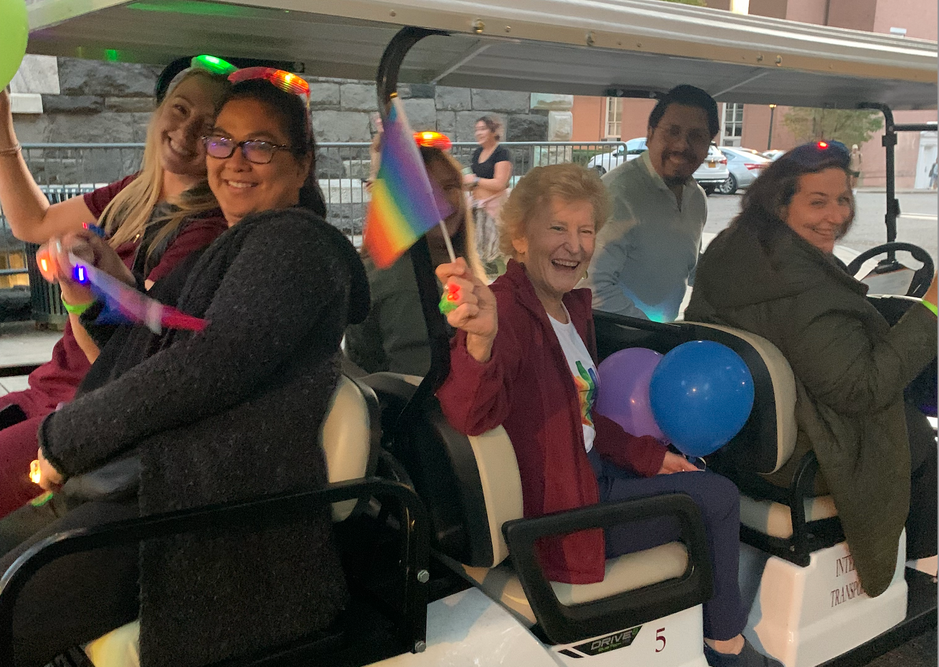 Joan in golf cart driving with pride flag