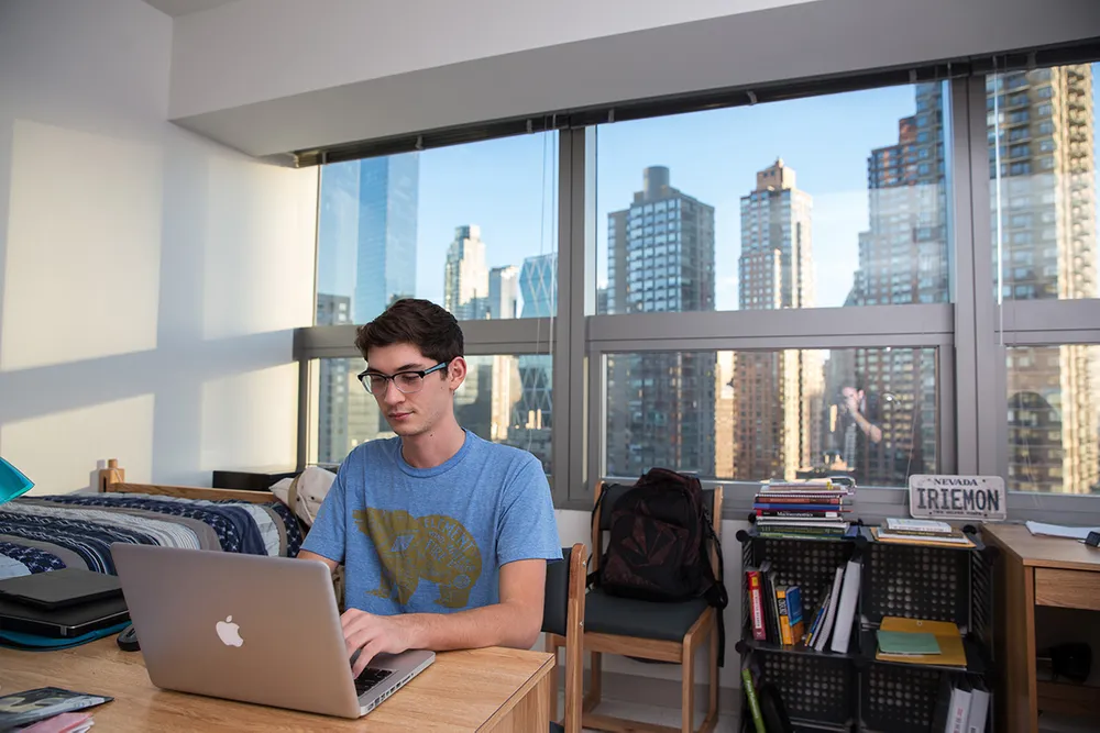 Male student works in his dorm with city skyline view out the window