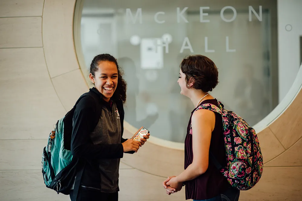 Two female students laughing in conversation in the hall