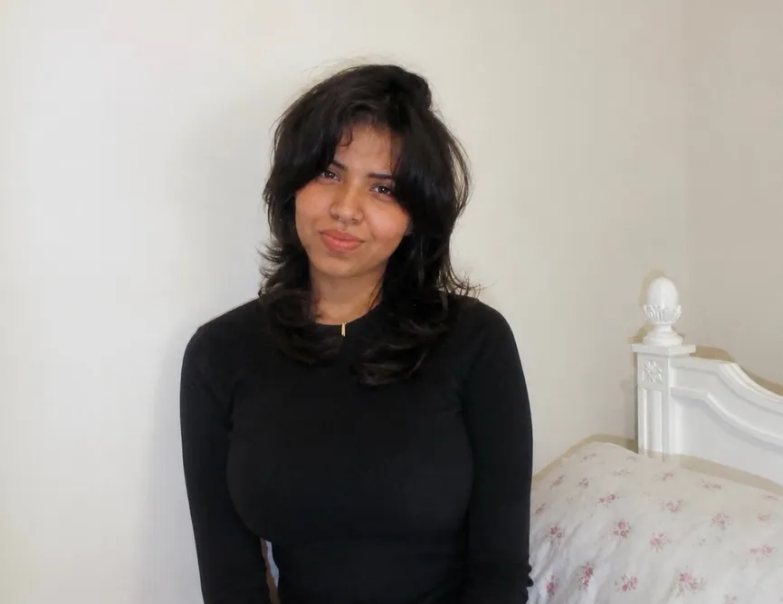 Angela sitting in her room in front of a white wall