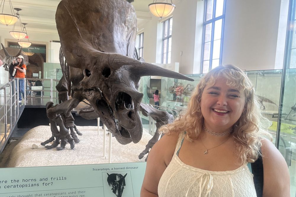 Aurora standing in front of a dinosaur fossil