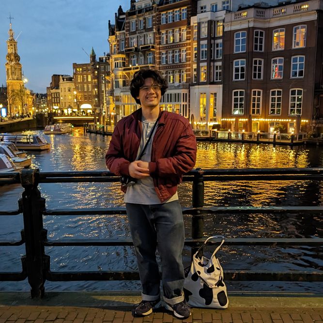 Student standing in front of a canal and buildings at night