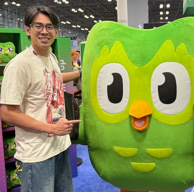 A student standing with the DuoLingo Owl