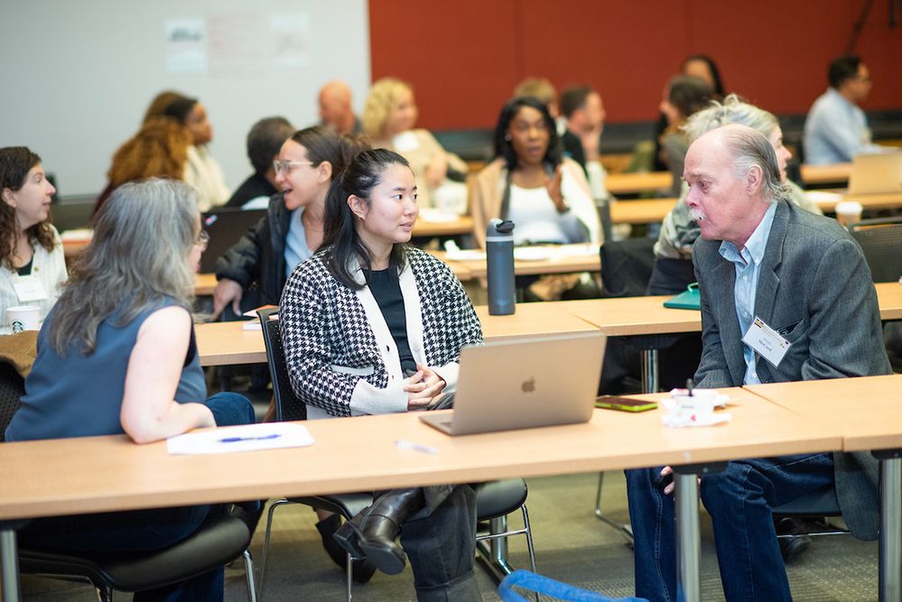 Three people talking while seated at a table in a classroom.