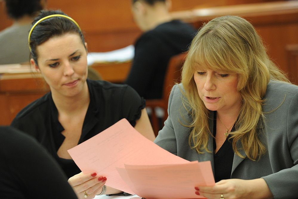 Two women reviewing pink documents in a classroom.