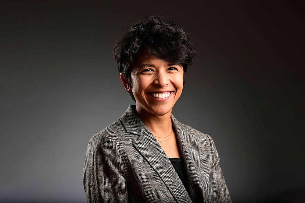 A woman with short wavy hair wearing a patterned blazer and black shirt.