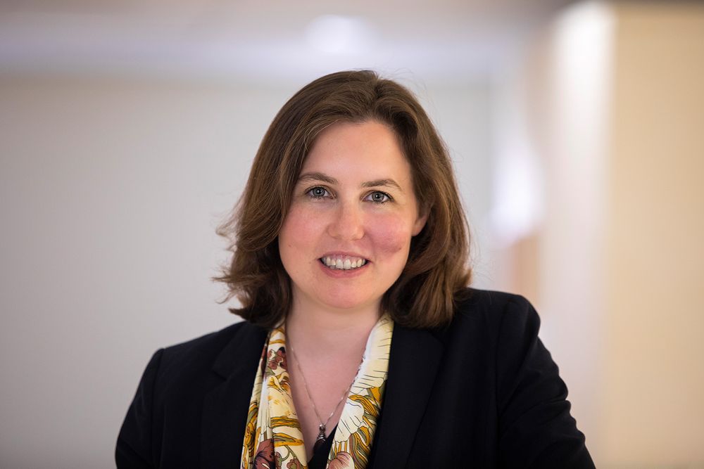 A woman wearing a black blazer and yellow patterned shirt.