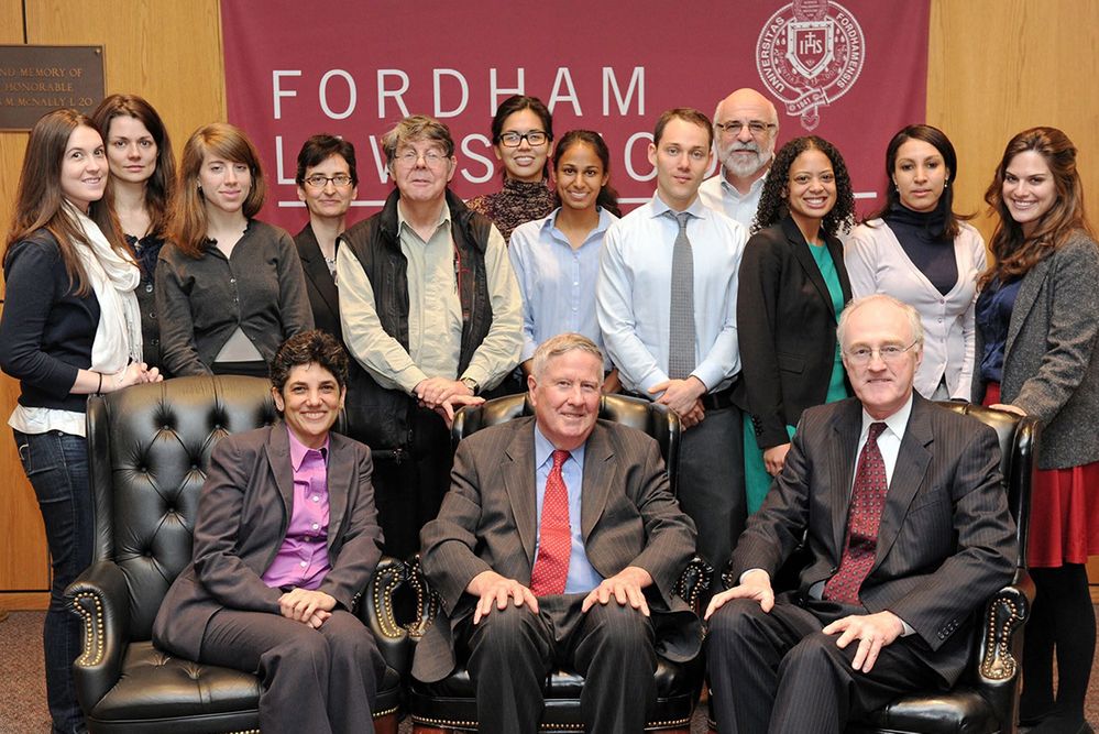 A group of adults standing and sitting in front of a banner.
