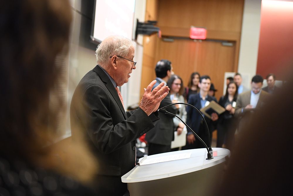 A man speaking at a podium to a lecture hall of attendees.