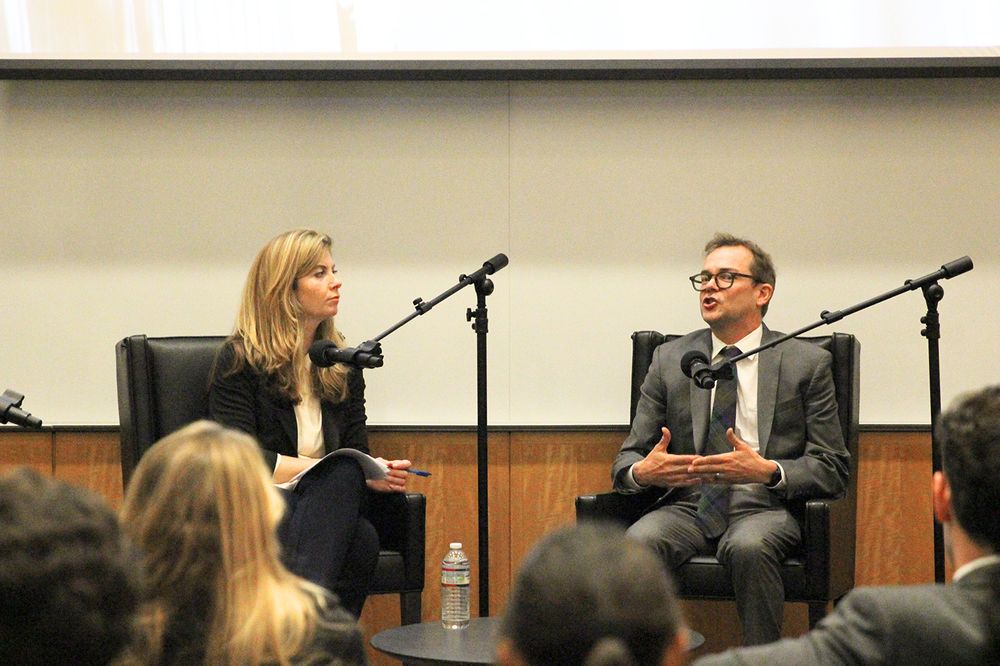 A woman and a man speaking into microphones on a stage.