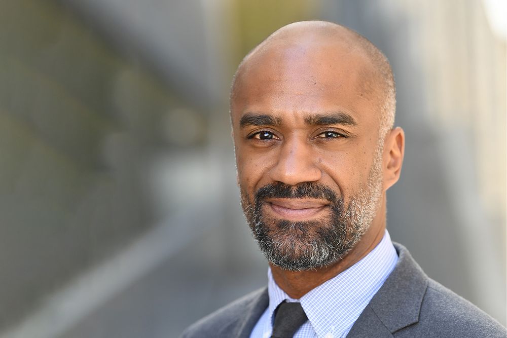 A man wearing a gray suit and blue-striped shirt.