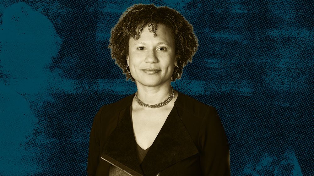 A woman with curly hair short hair wearing a black blazer against a blue textured background.