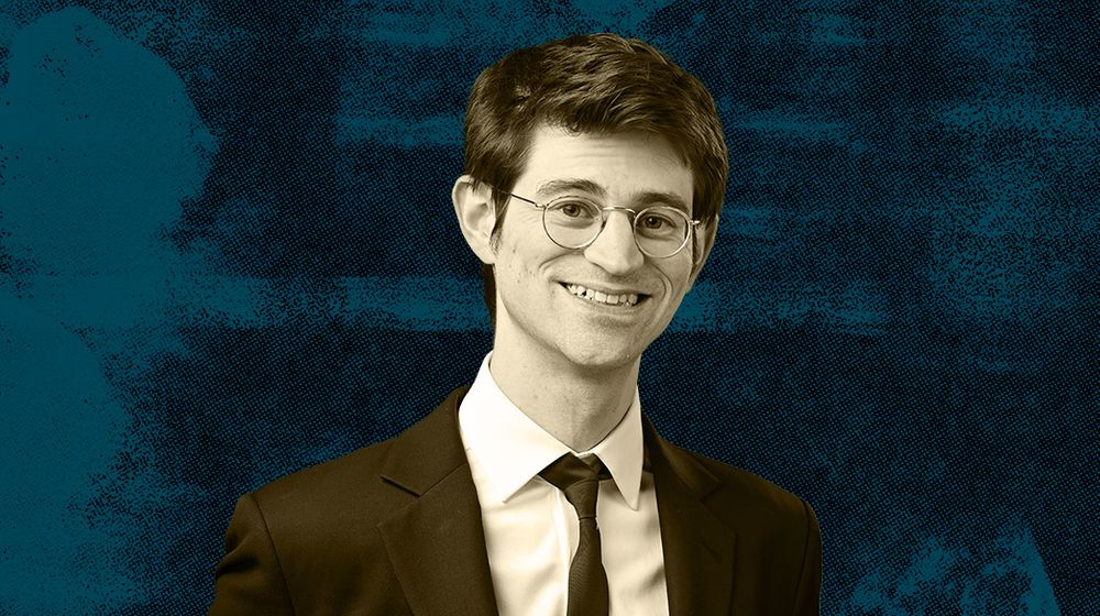 A man wearing glasses and a suit against a blue textured background.