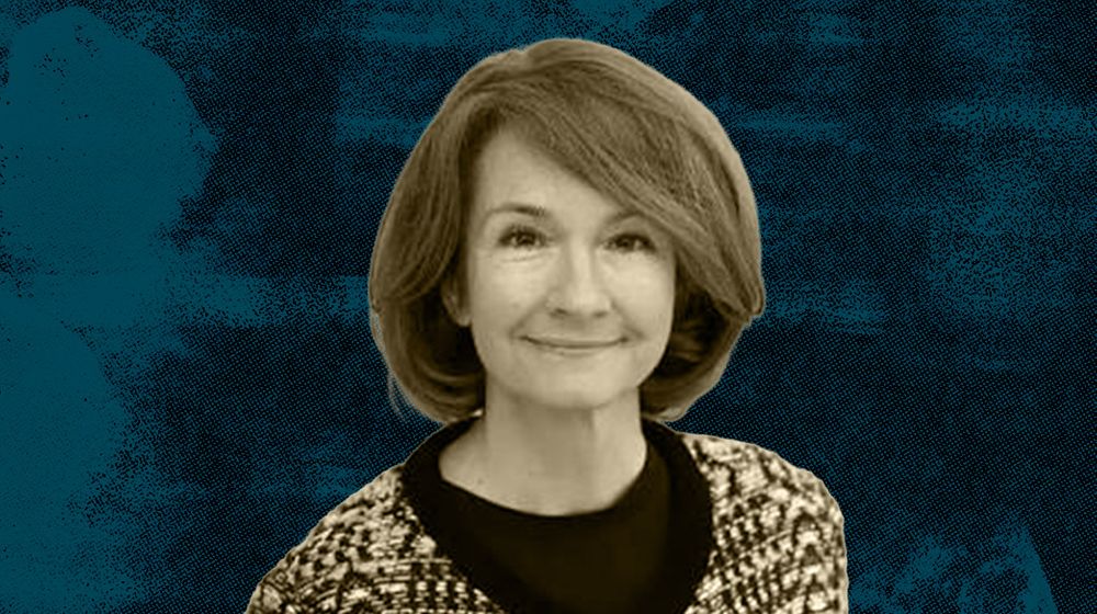 A woman with short hair wearing a patterned sweater against a blue textured background.