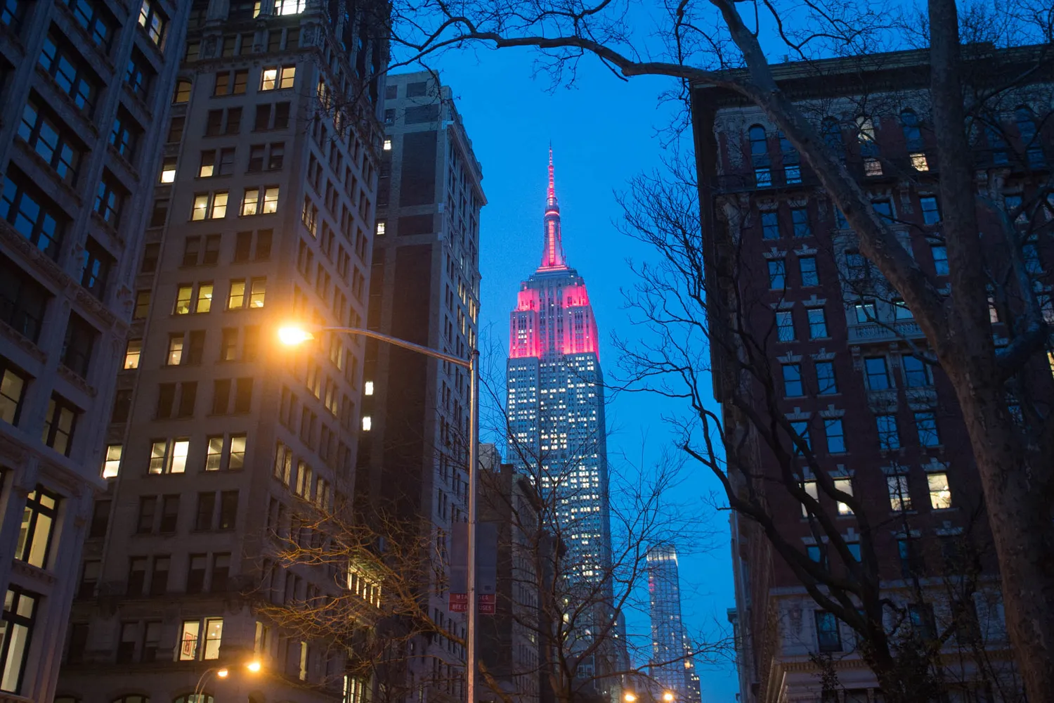 Empire State building lit up in maroon. Buildings surrounding it.