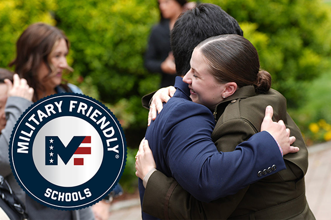 Two people in military uniform embracing at a Fordham campus event, with the Military Friendly Schools badge overlaid.