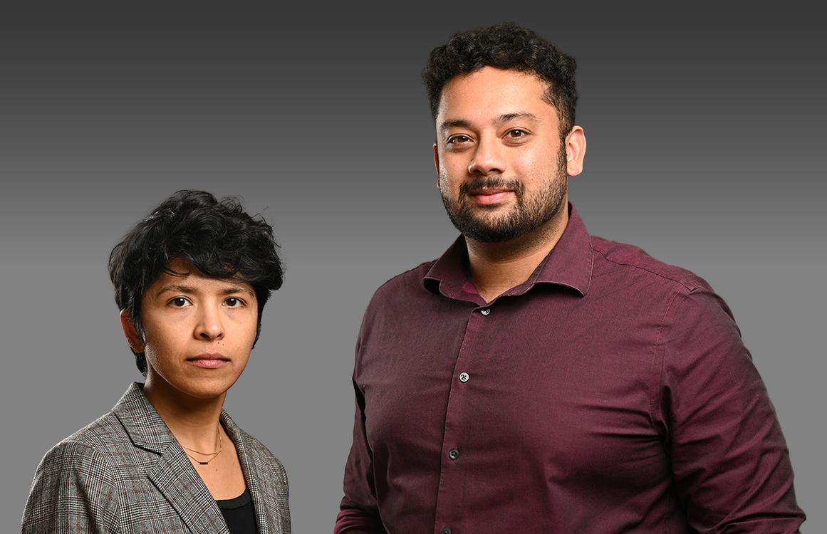 A man and a woman standing together against a gray backdrop.