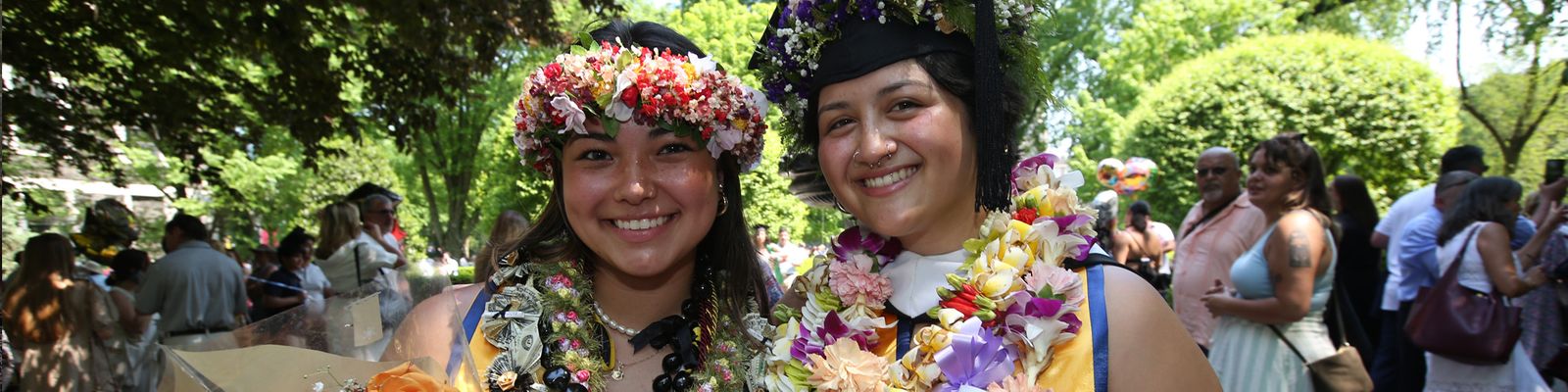 Two female students smiling with decorated graduation caps at Fordham Commencement