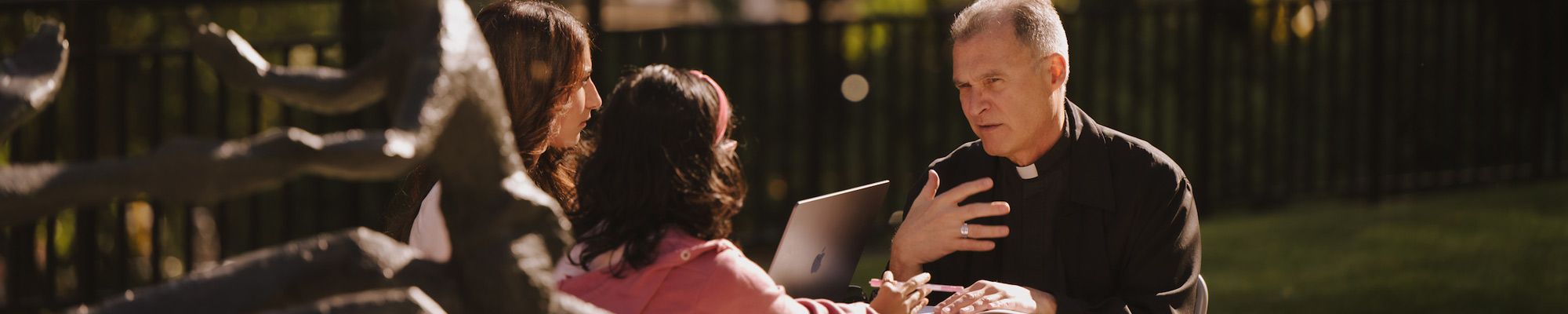 Jesuit teaching two student on the plaza at LC