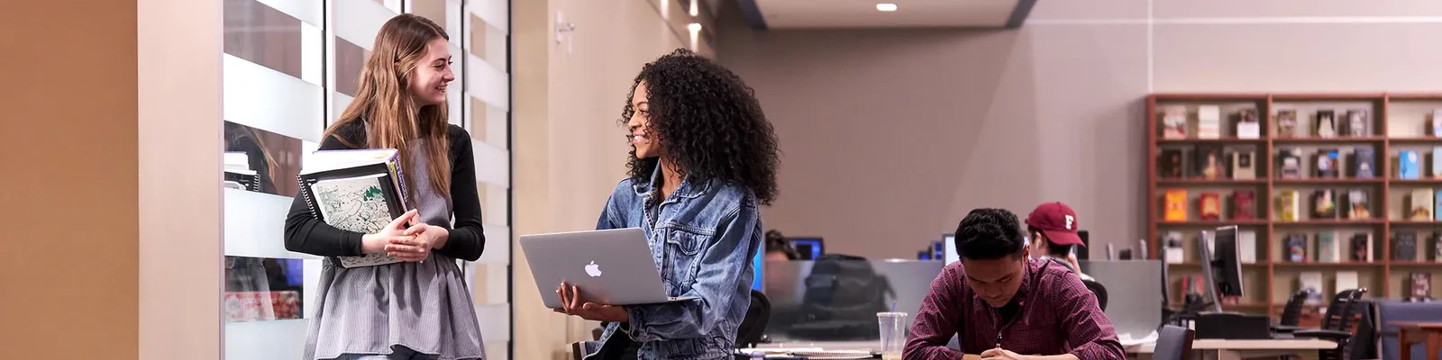 Students talking in library holding a laptop