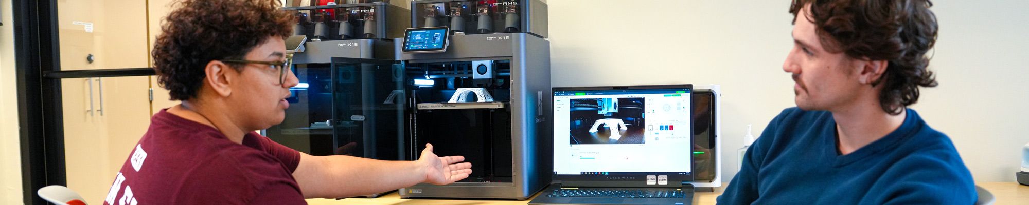 Two students discuss a project built with a 3-D printer