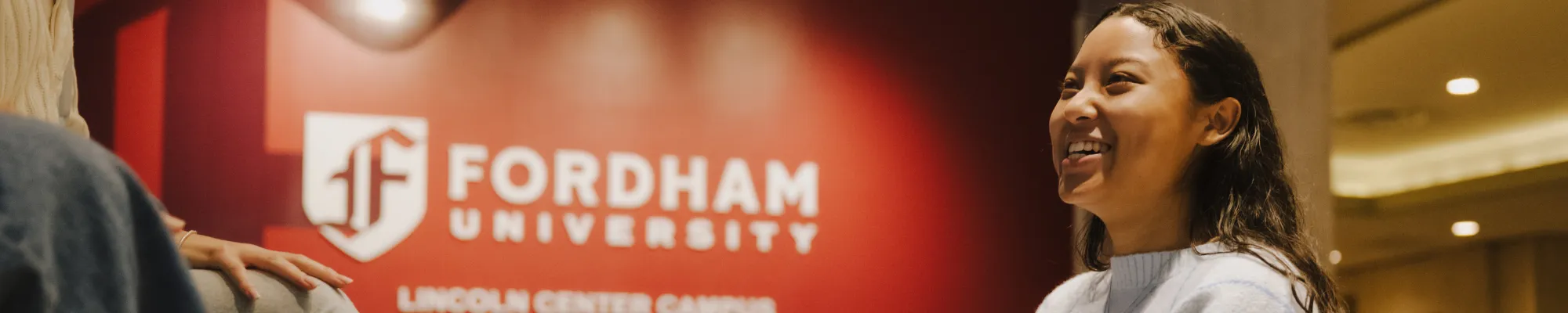 student sitting in front of a Fordham sign and laughing