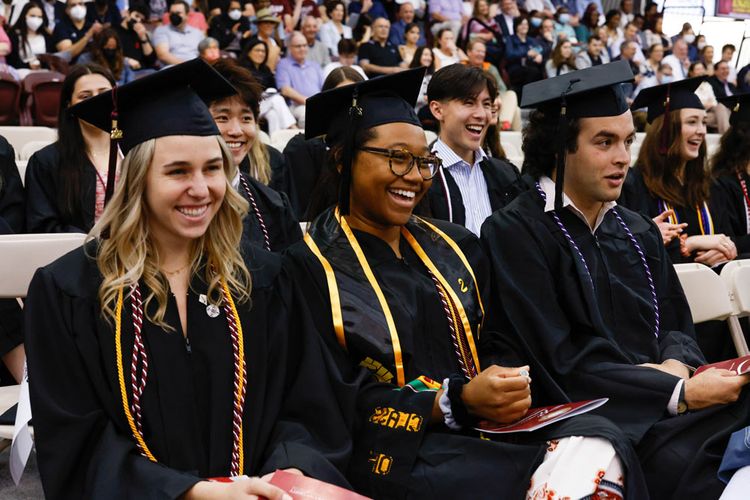 Students wearing caps and gowns at Commencement smile