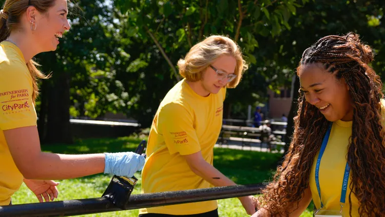 3 Fordham students in Urban Plunge painting a park bench