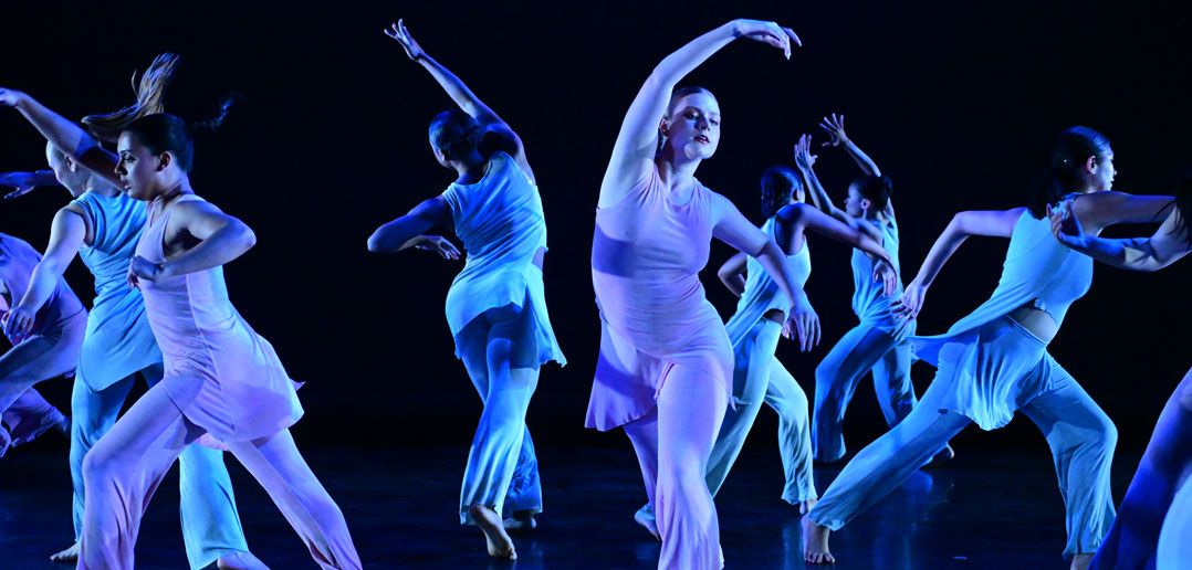 Dancers draped in blue light are dancing together on stage