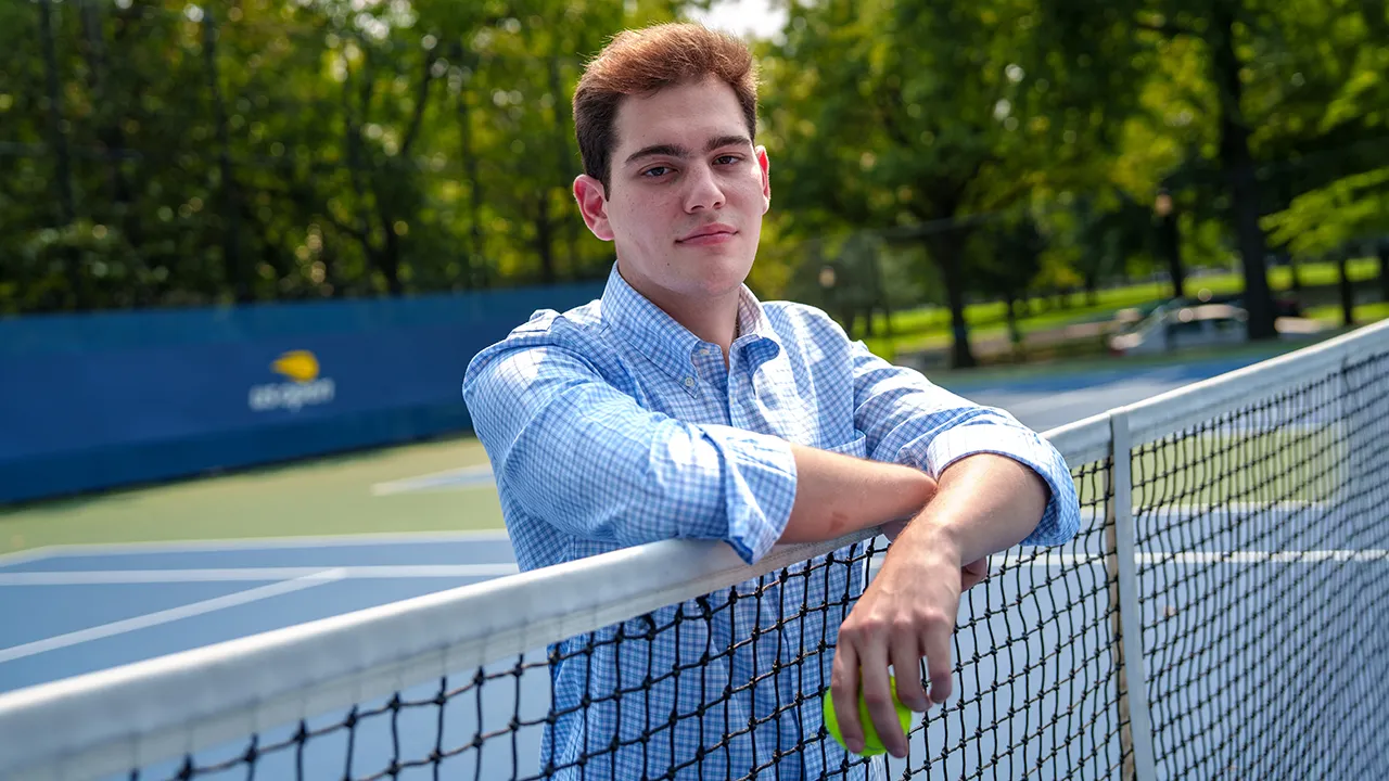 A student poses on a tennis net
