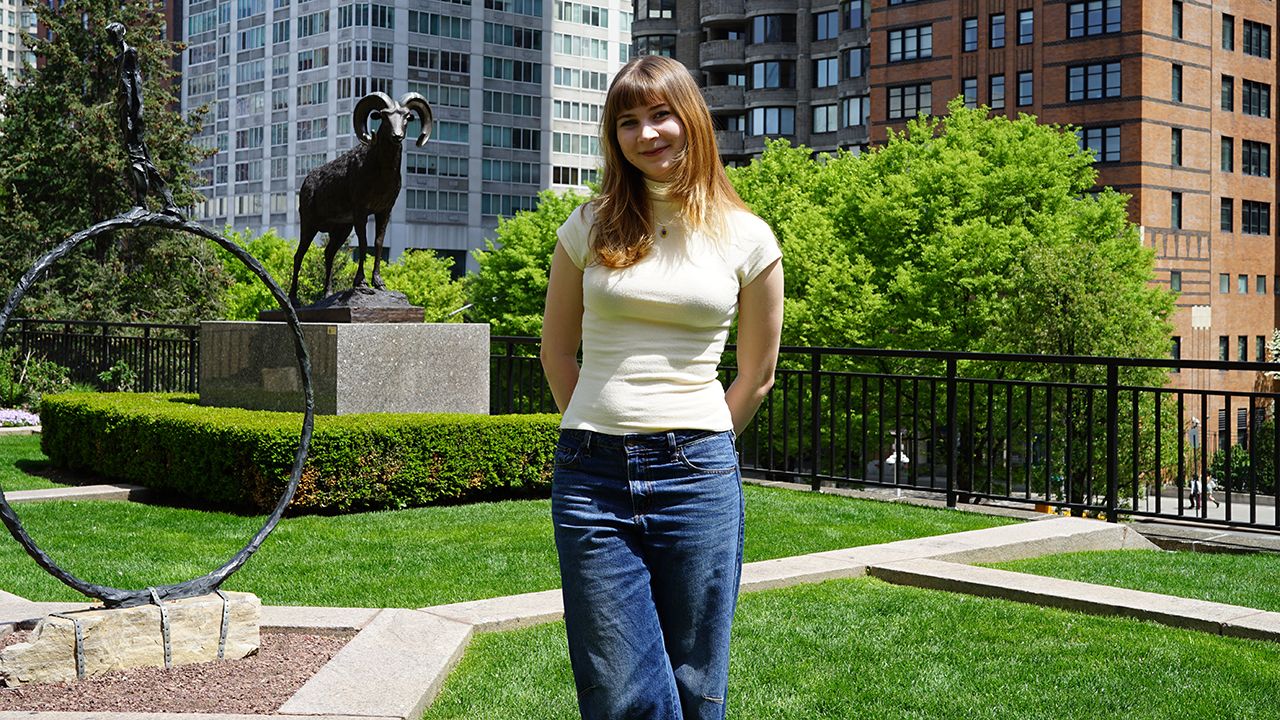 A student poses on the plaza in front of a ram statue