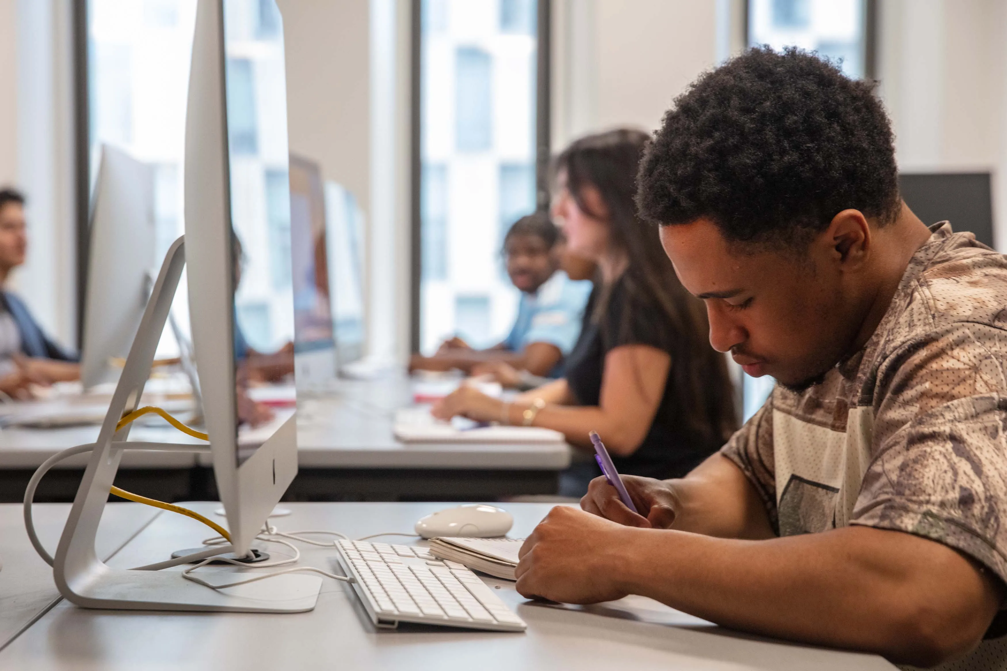 student writing in notebook at computer desk
