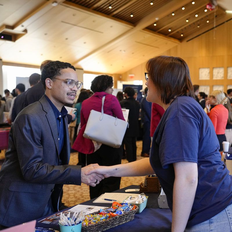 A male student shakes hands with a job recruiter at an on-campus career fair