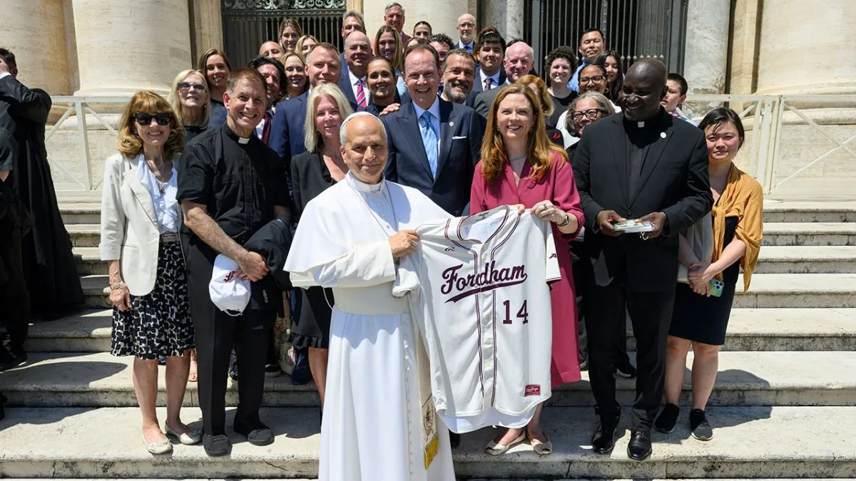 Pope Leo holds up a Fordham jersey posing with a group of Fordham faculty, administrators, and trustees in Rome.