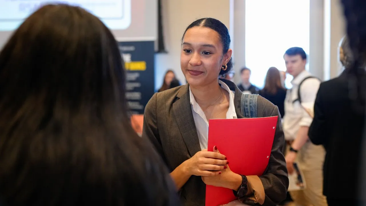 A female student holding her resume talks to a job recruiter at a career fair