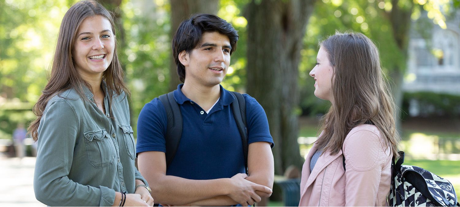 Female and Male Student in a Group Talking, One Female Student Smiling at Camera.